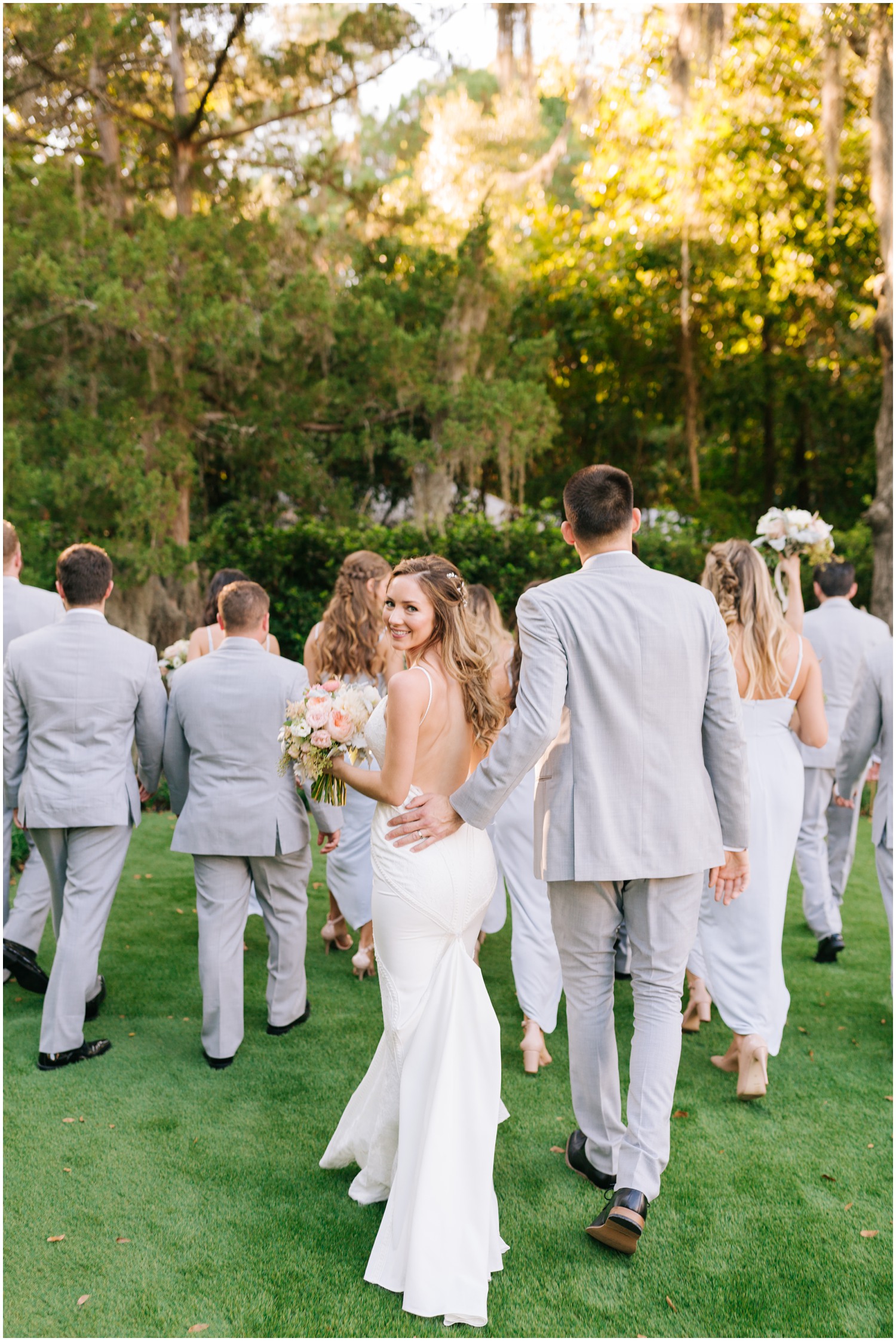 bride and groom walk with bridal party while bride looks over shoulder