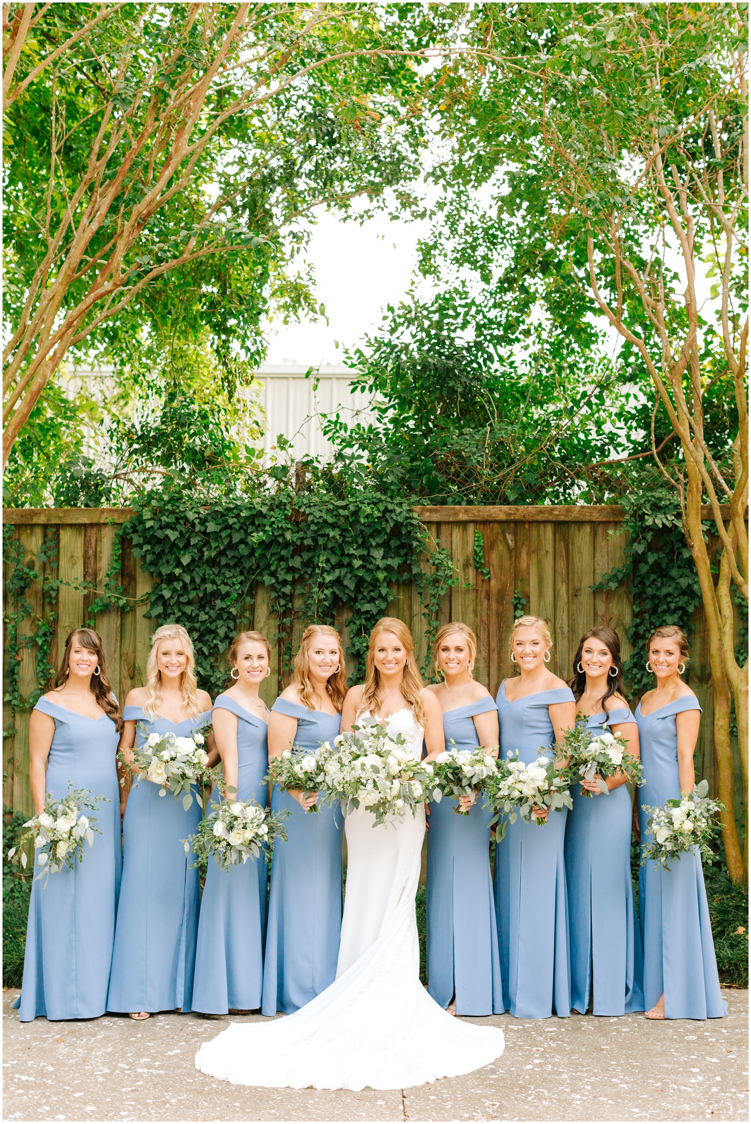 bride poses with 8 bridesmaids in dusty blue dresses