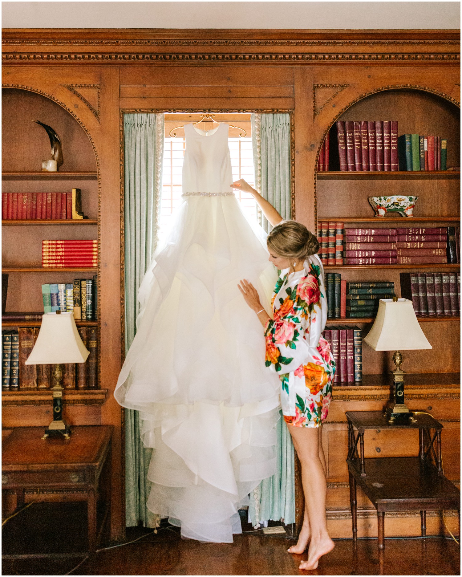bride looks at wedding gown hanging in window of library in Graylyn Estate