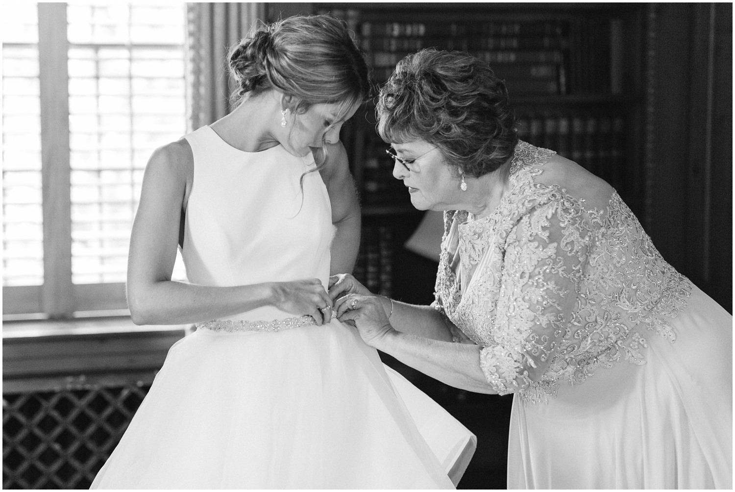 mother helps bride adjust belt on wedding dress