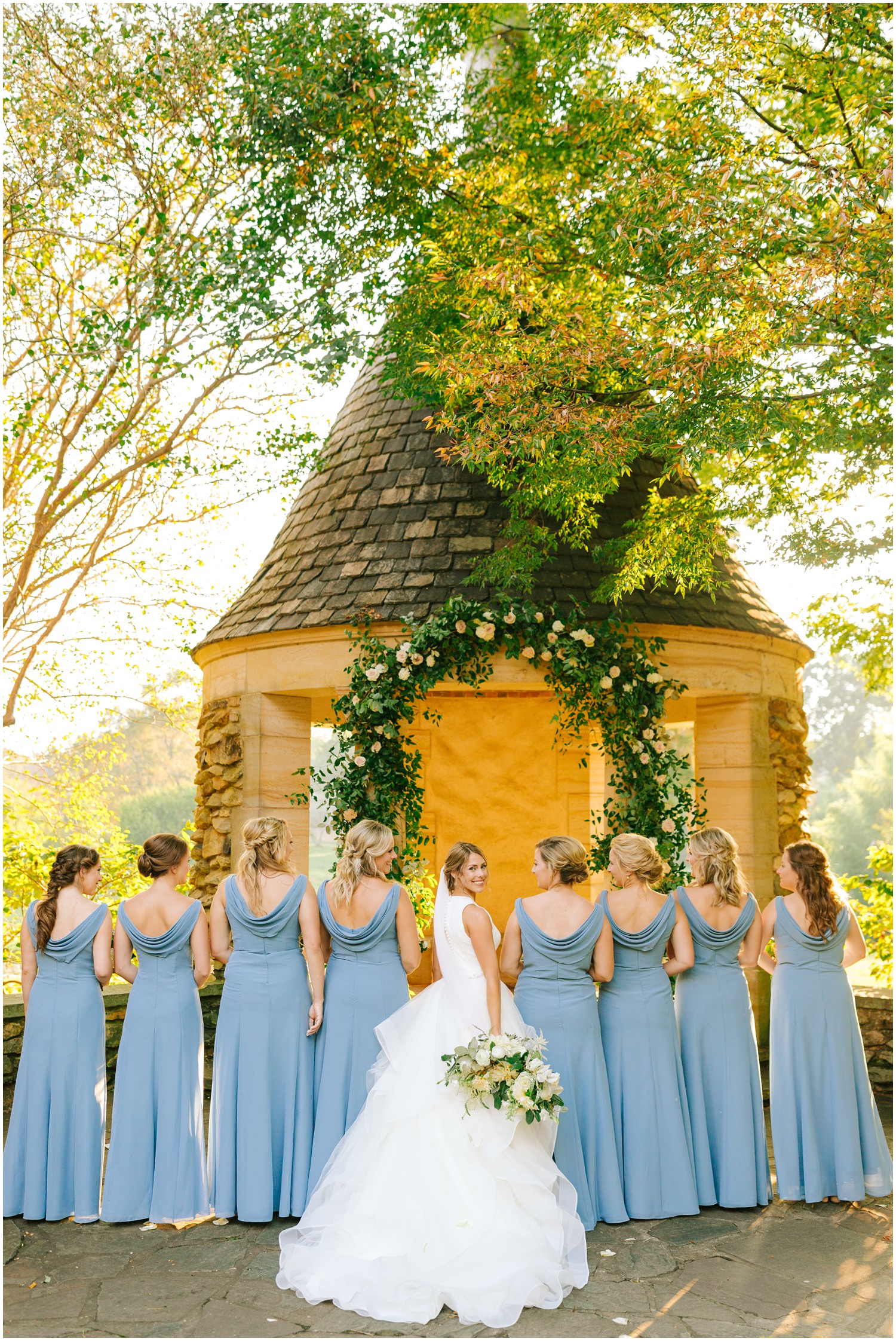 bride looks over shoulder at Chelsea Renay Photography while 8 bridesmaids in blue gowns look at her