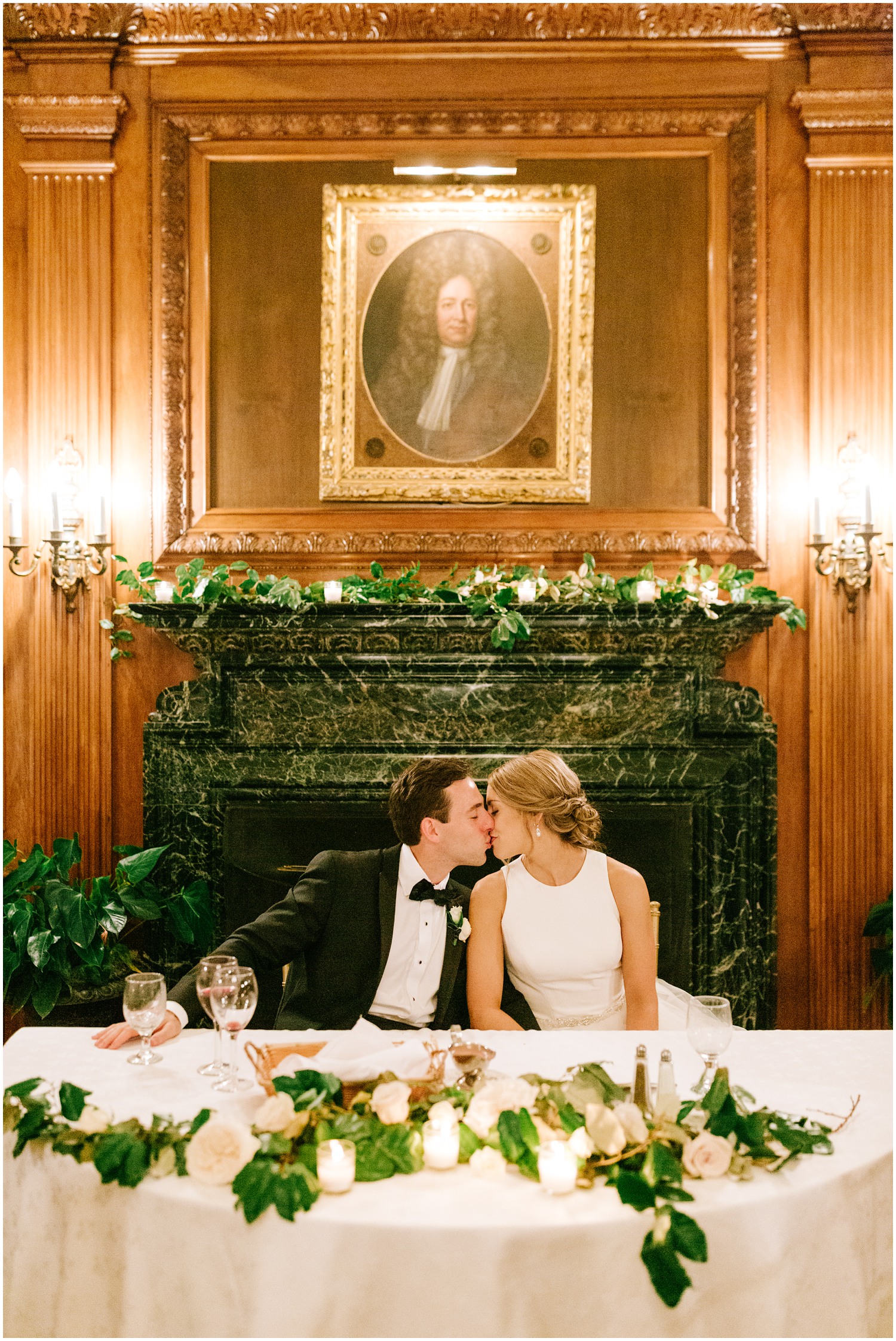 bride and groom kiss at sweetheart table decorated with ivy and candles at Graylyn Estate