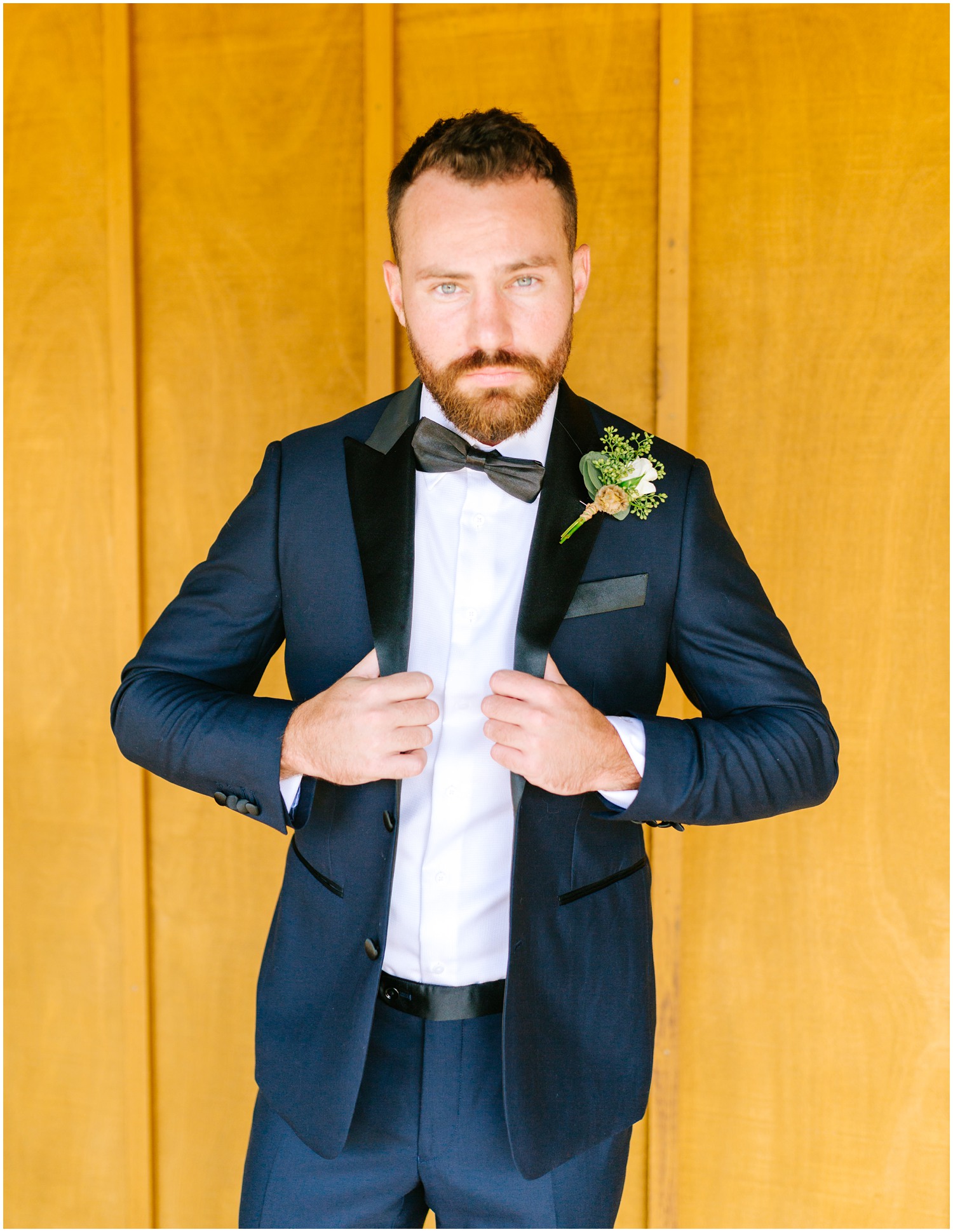 groom adjusts suit in front of wooden paneled wall