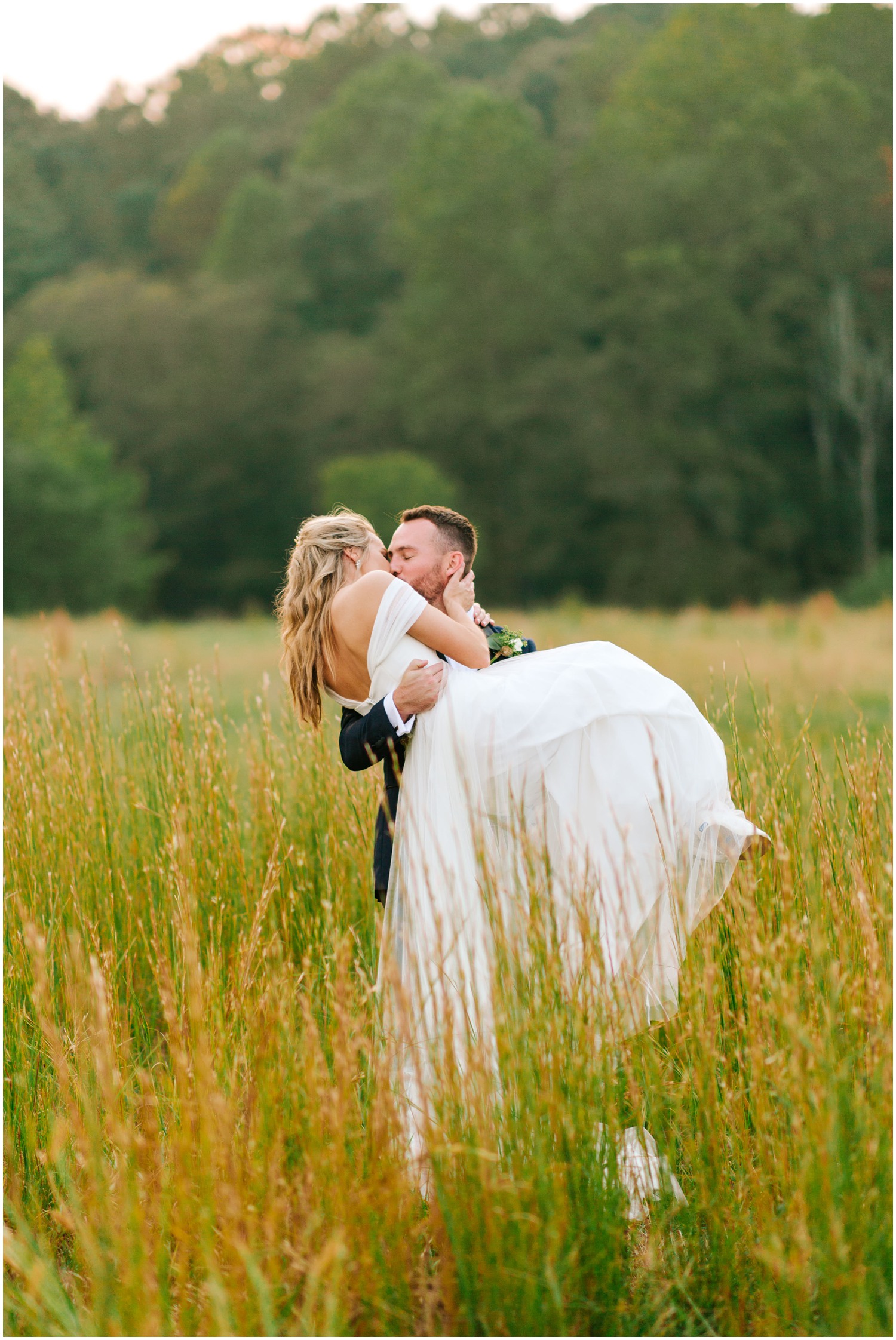 groom lifts bride up while standing in field photographed by Chelsea Renay