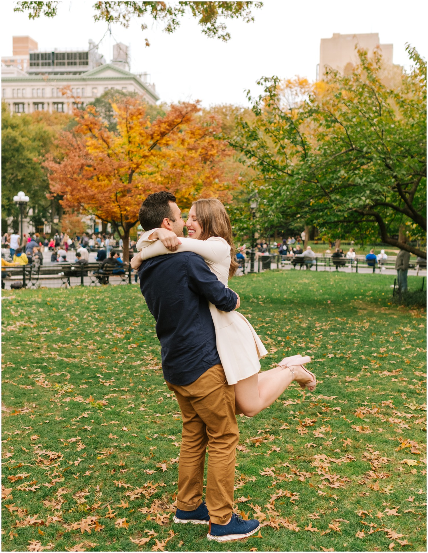 groom lifts bride in ivory dress up with fall trees in background