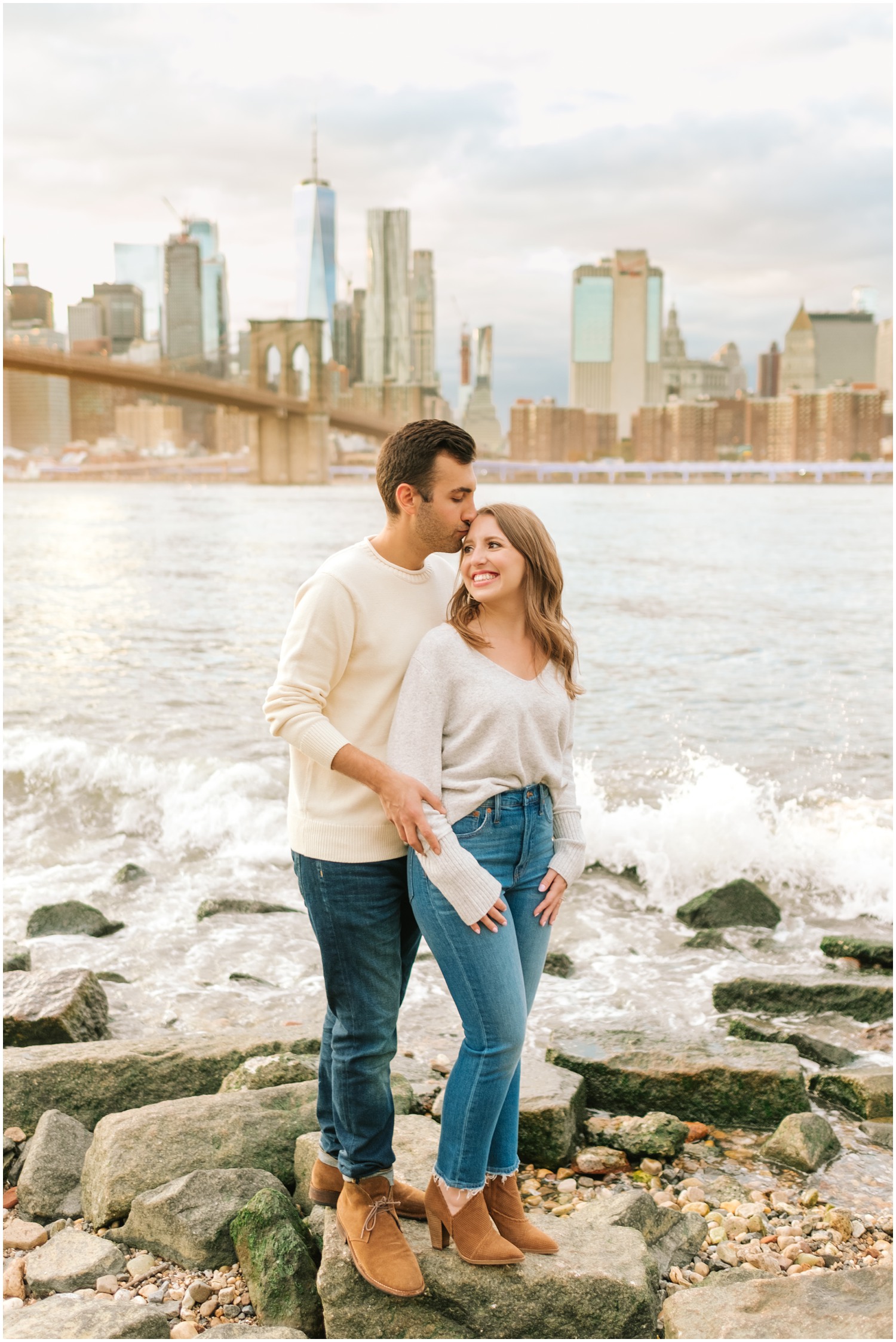 groom kisses bride's forehead while water crashes behind them from Hudson River