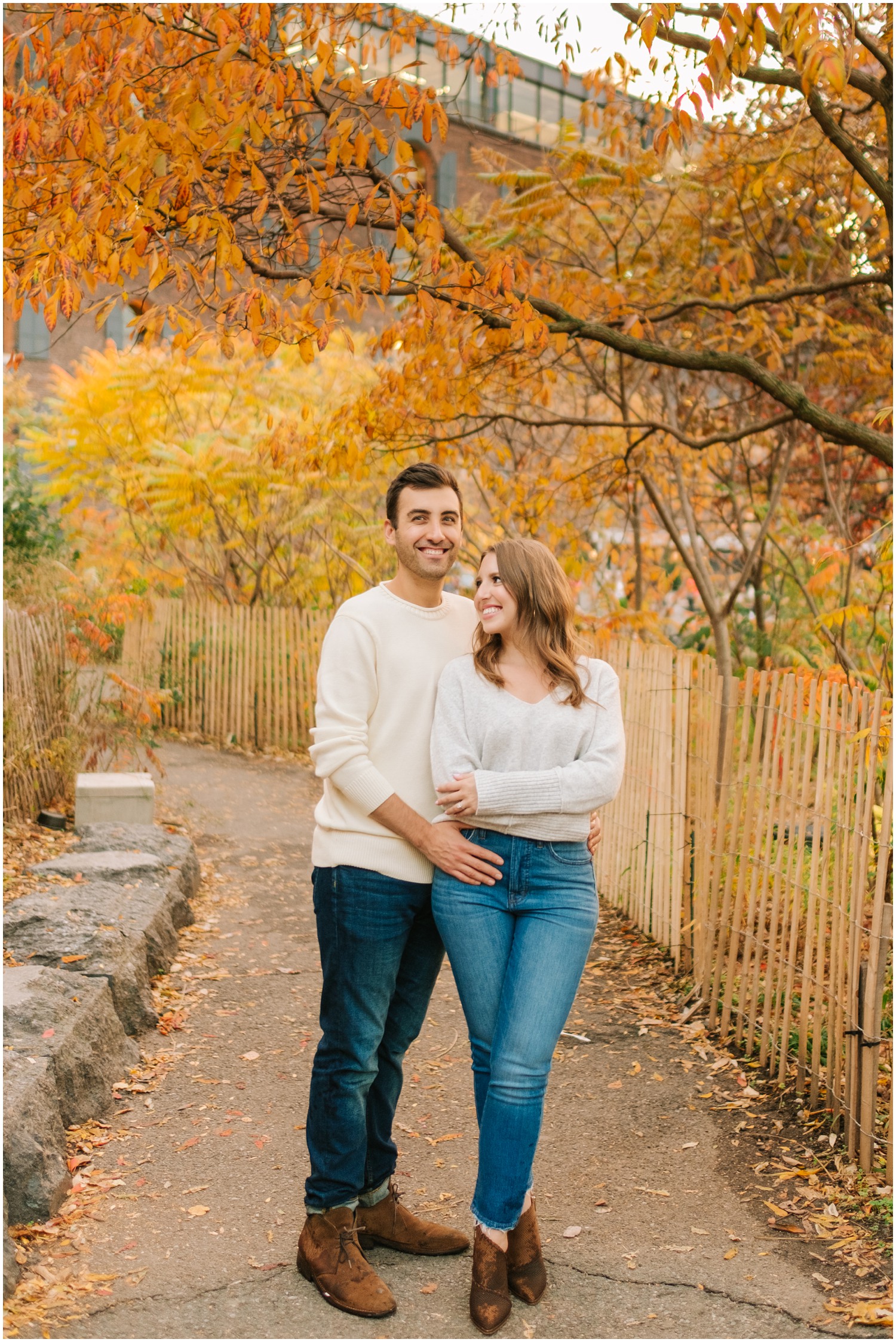 bride in sweater and jeans leans against groom during fall engagement session in NYC