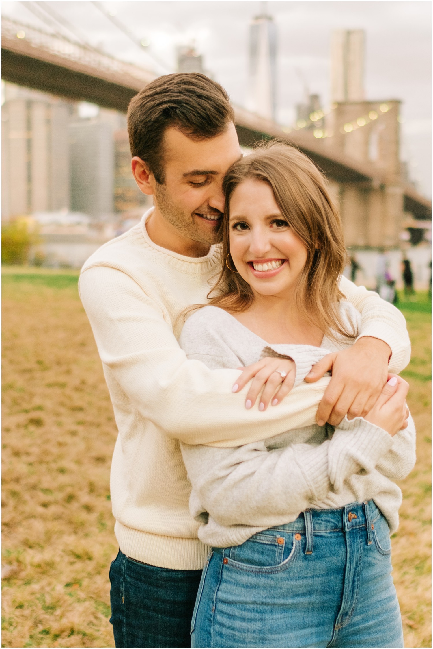 groom hugs bride from behind in DUMBO by Brooklyn Bridge