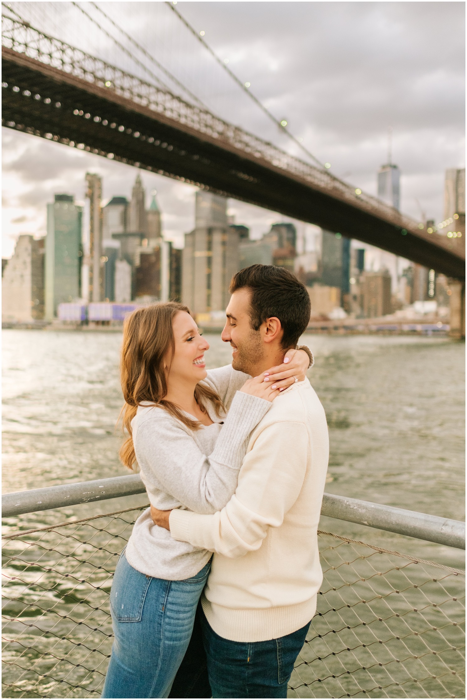 couple hugs and smiles by the Brooklyn Bridge in New York City