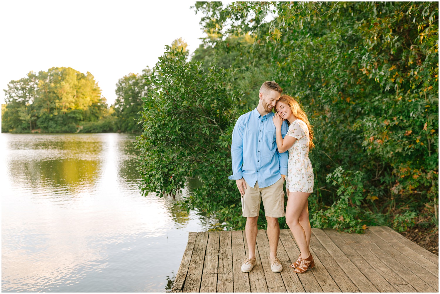 engaged couple stands by lake on dock