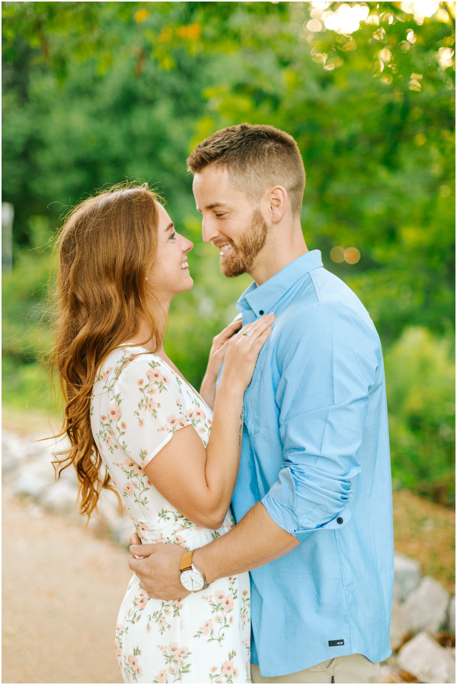 bride smiles at groom during engagement photos with hands resting on his chest