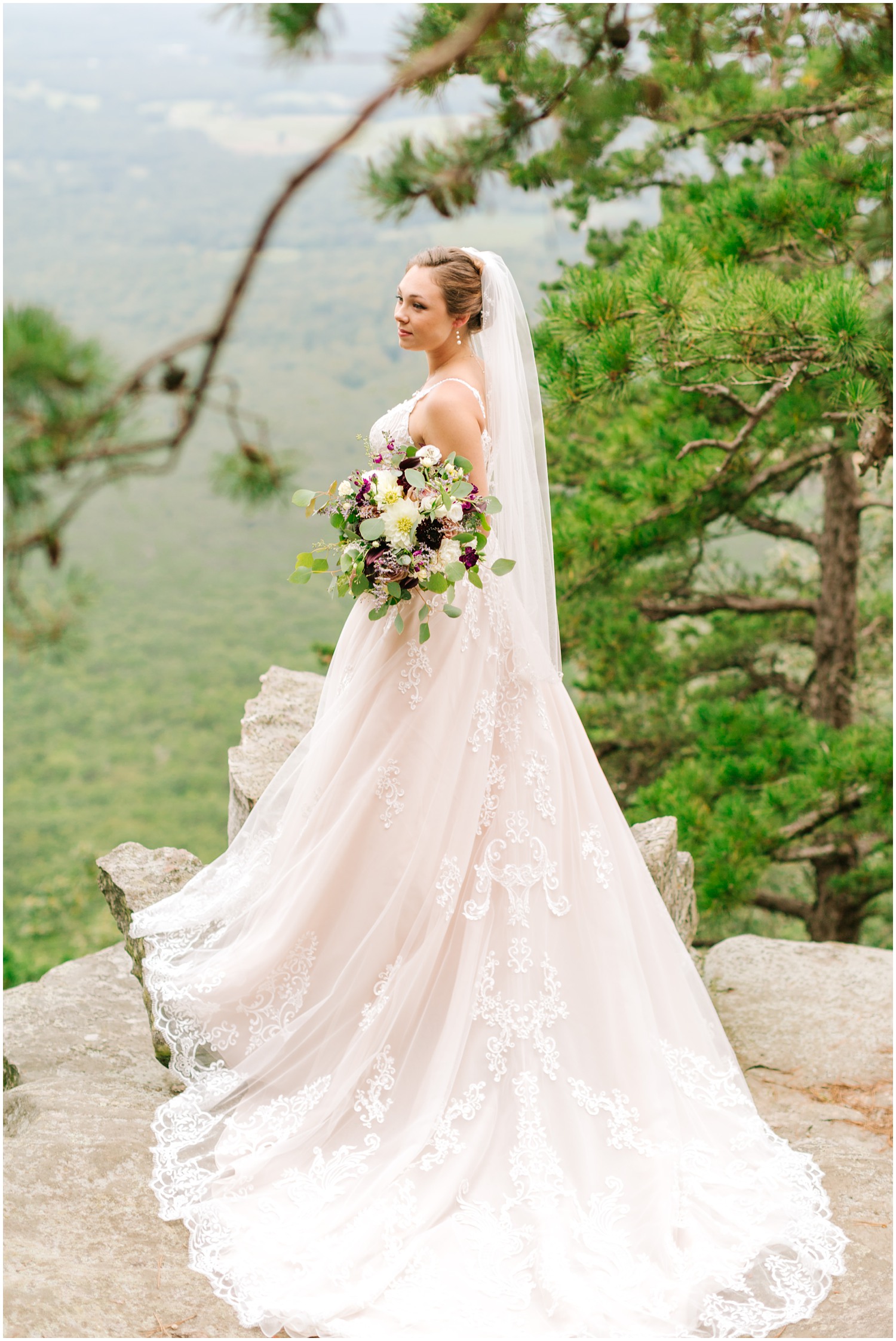 bride holds bouquet by hip with dress laid out behind her showing off lace detail