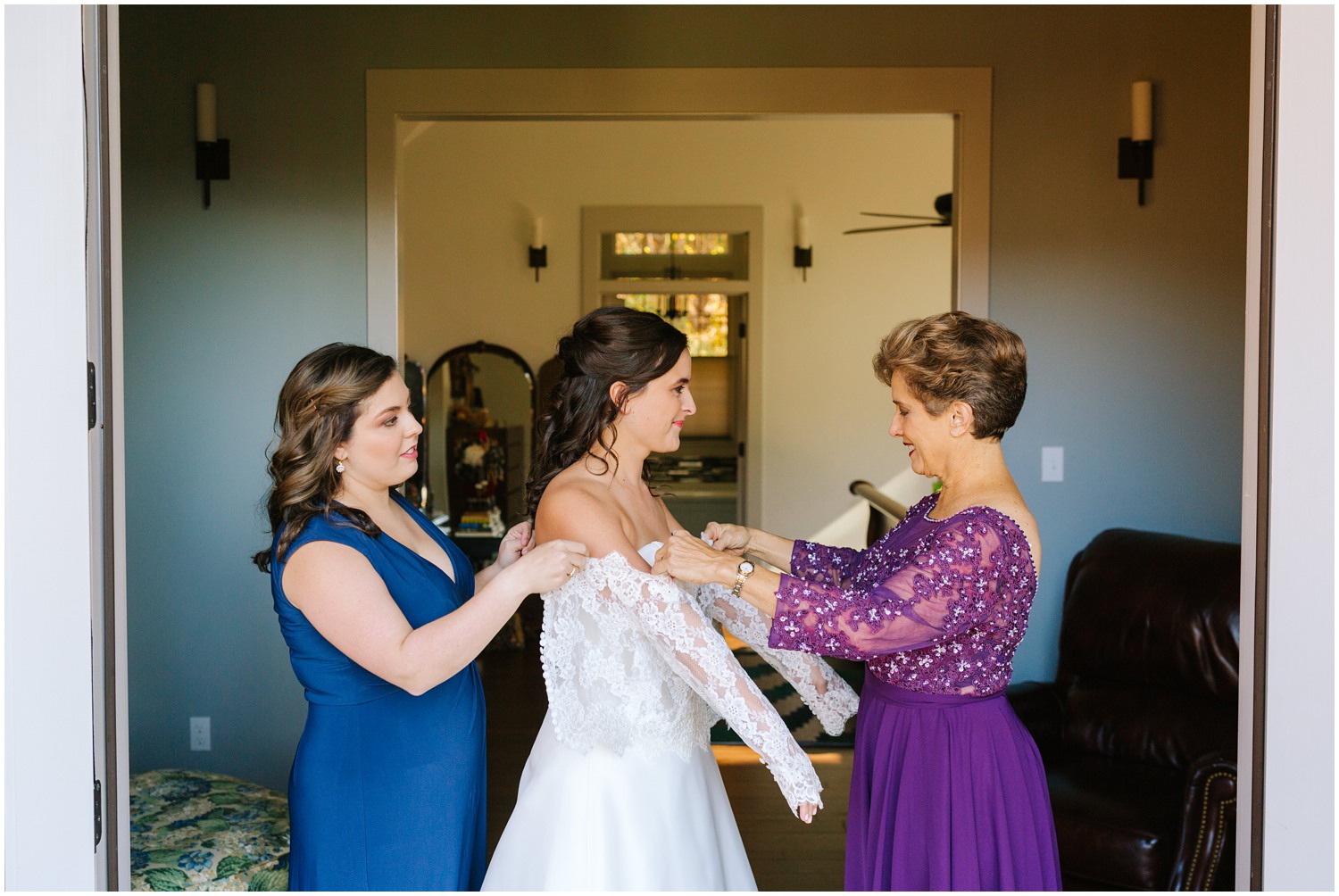 bridesmaid and mother of the bride help bride put on lace sleeves for wedding dress