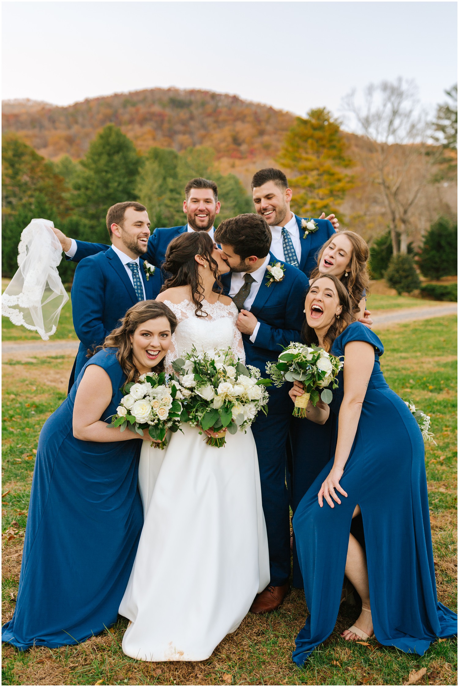 bridal party laughs while bride and groom kiss