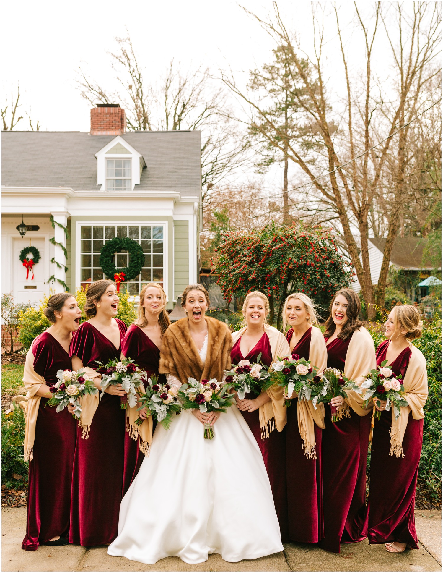 bridesmaids in burgundy velvet gowns pose with bride outside childhood home photographed by Chelsea Renay Photography