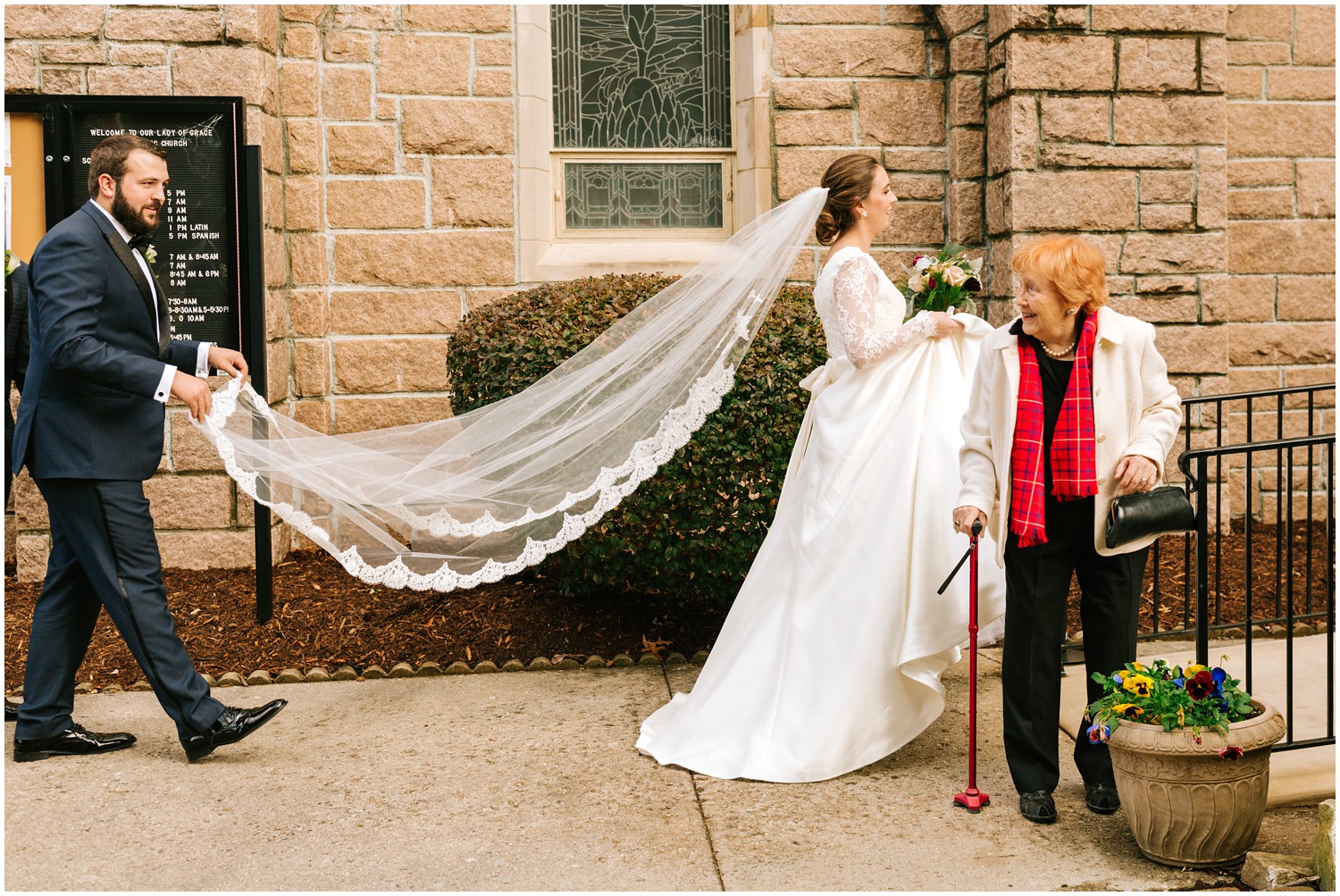 groomsman carries bride's veil while talking to guest
