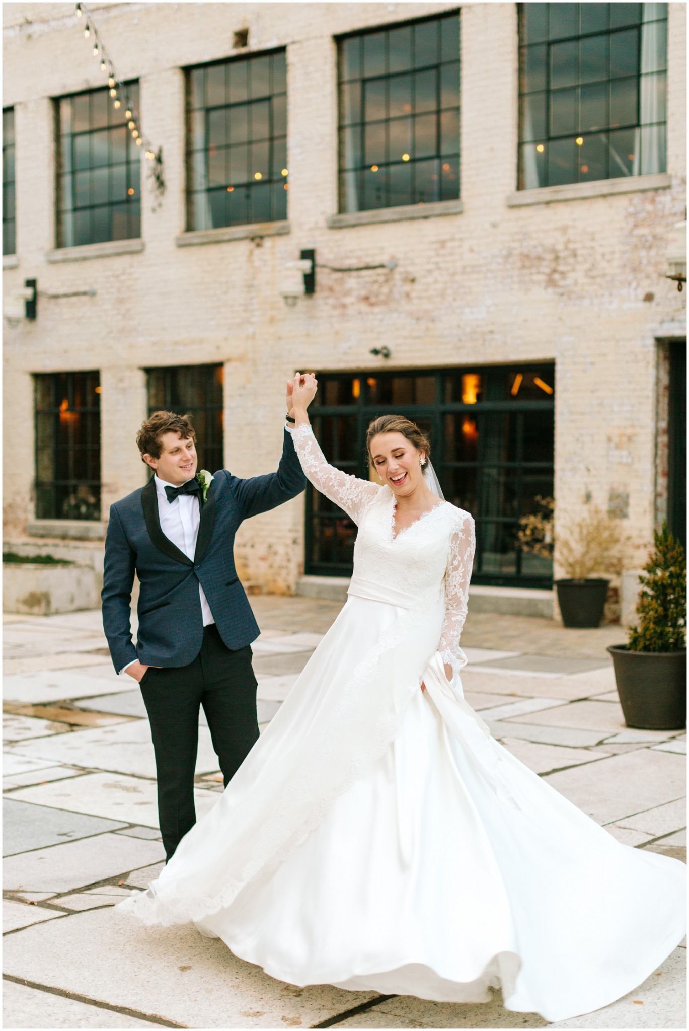 groom twirls bride in wedding gown with long lace sleeves and veil