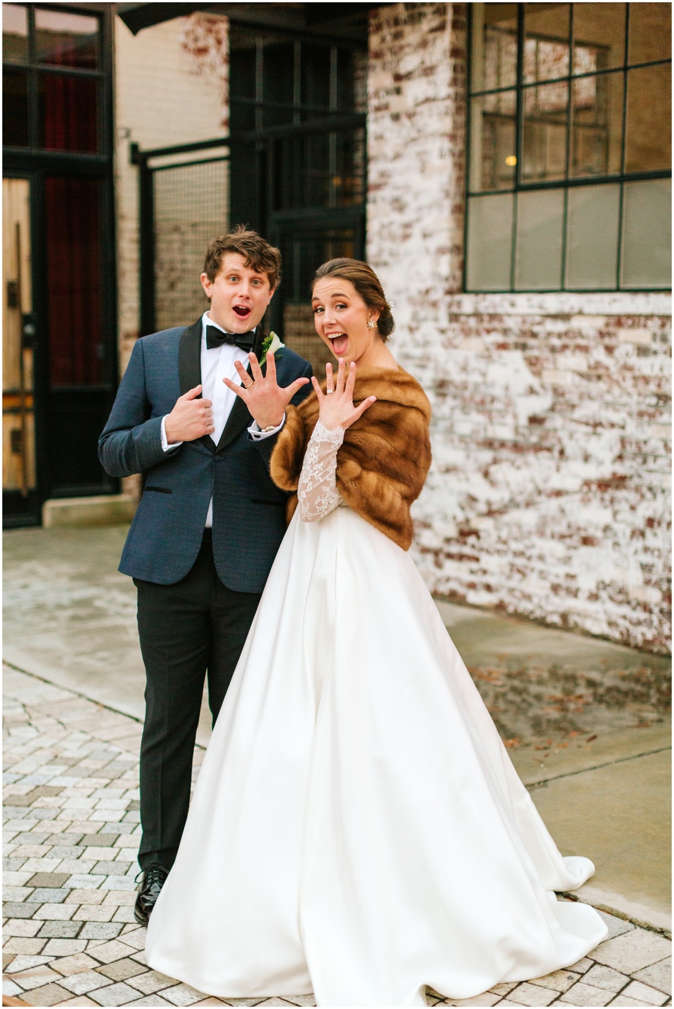 groom in navy blue suit and bride with brown fur show off wedding rings to Chelsea Renay Photography