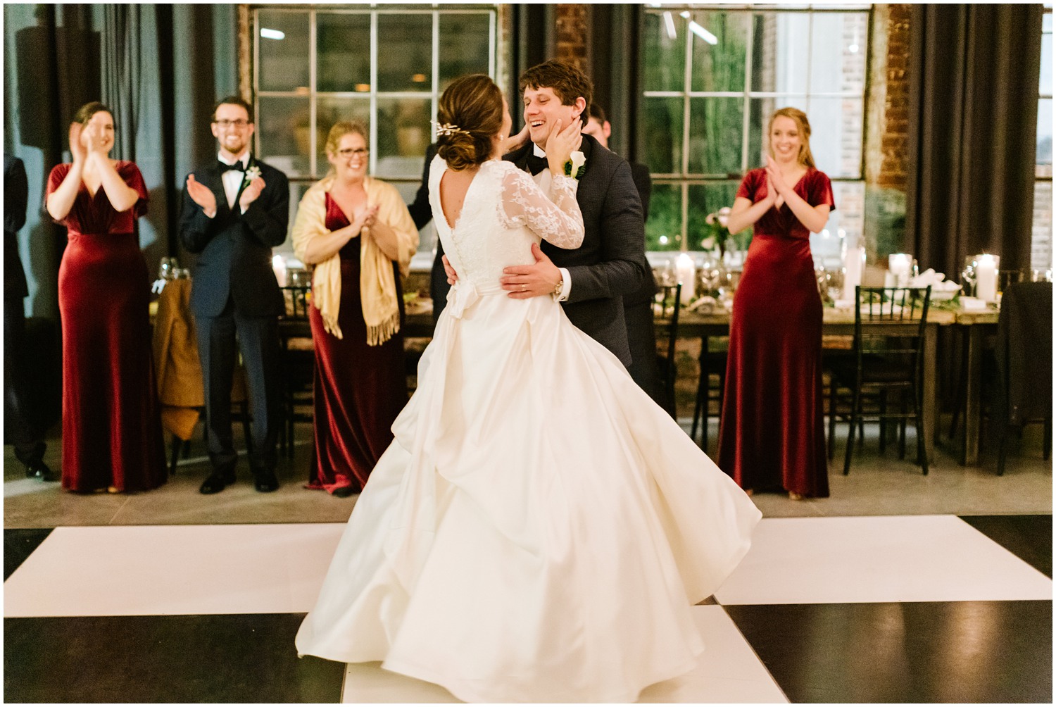 bride in long lace sleeve wedding gown smiles at new husband on black and white checkered dance floor