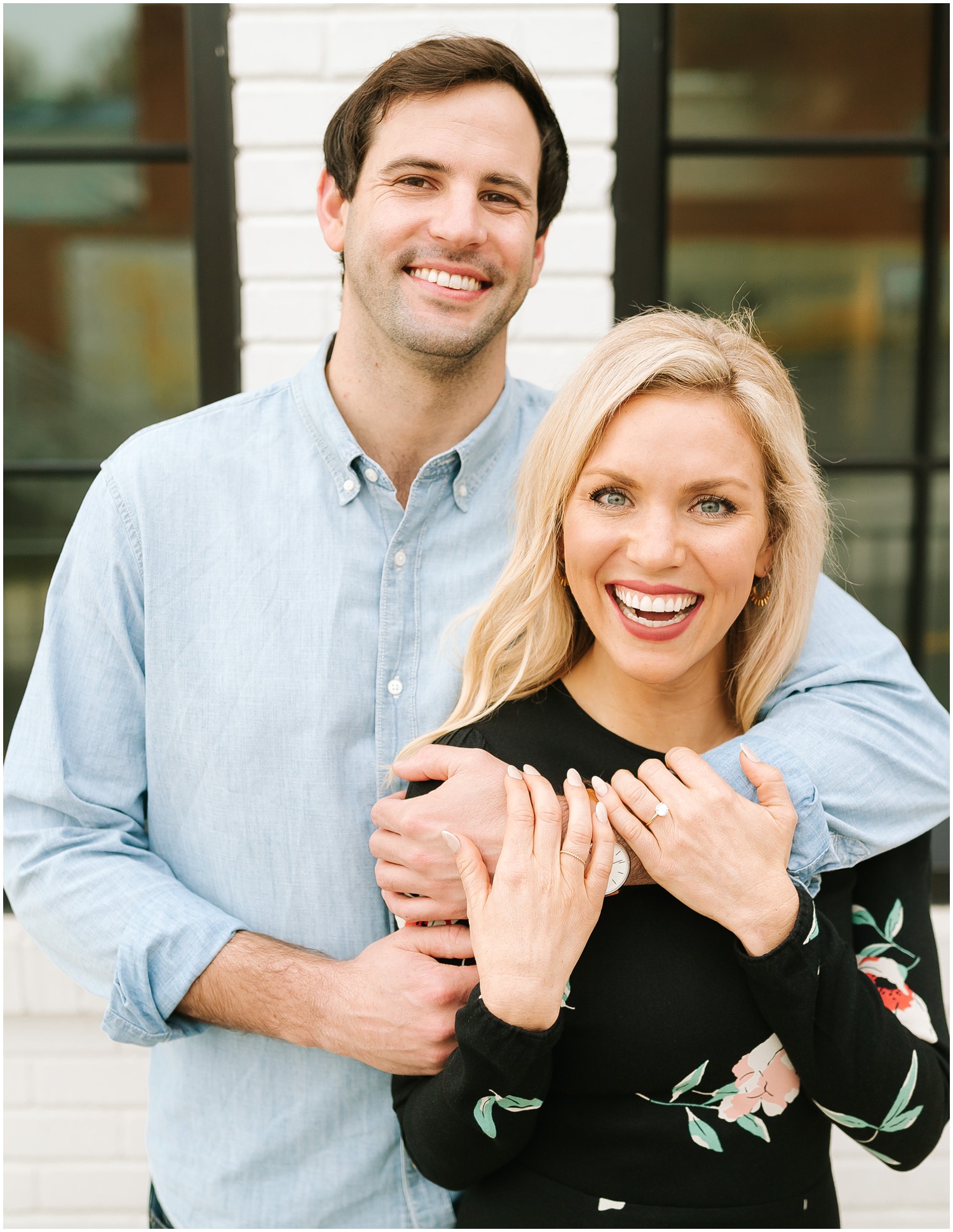 engaged couple embraces next to white brick wall in Raleigh NC