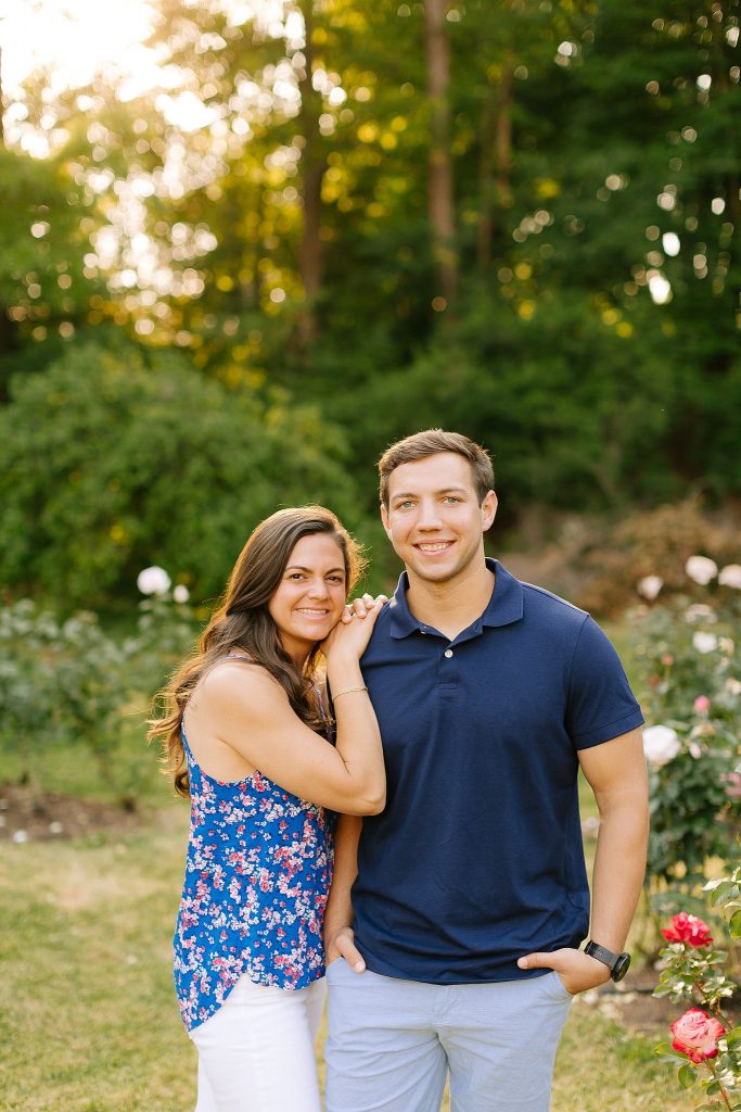 bride in blue floral shirt leans against groom in navy polo at Raleigh Rose Garden engagement session
