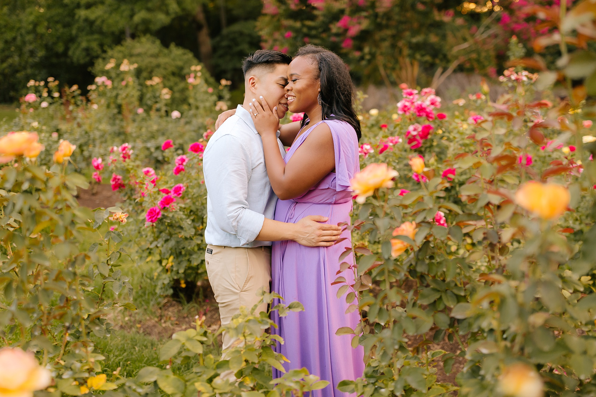 groom kisses bride to be on the cheek during garden engagement session