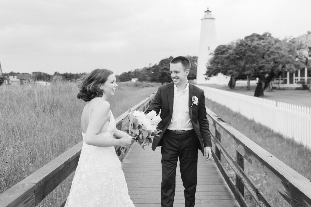 bride and groom laugh on walkway in front of Ocracoke Lighthouse