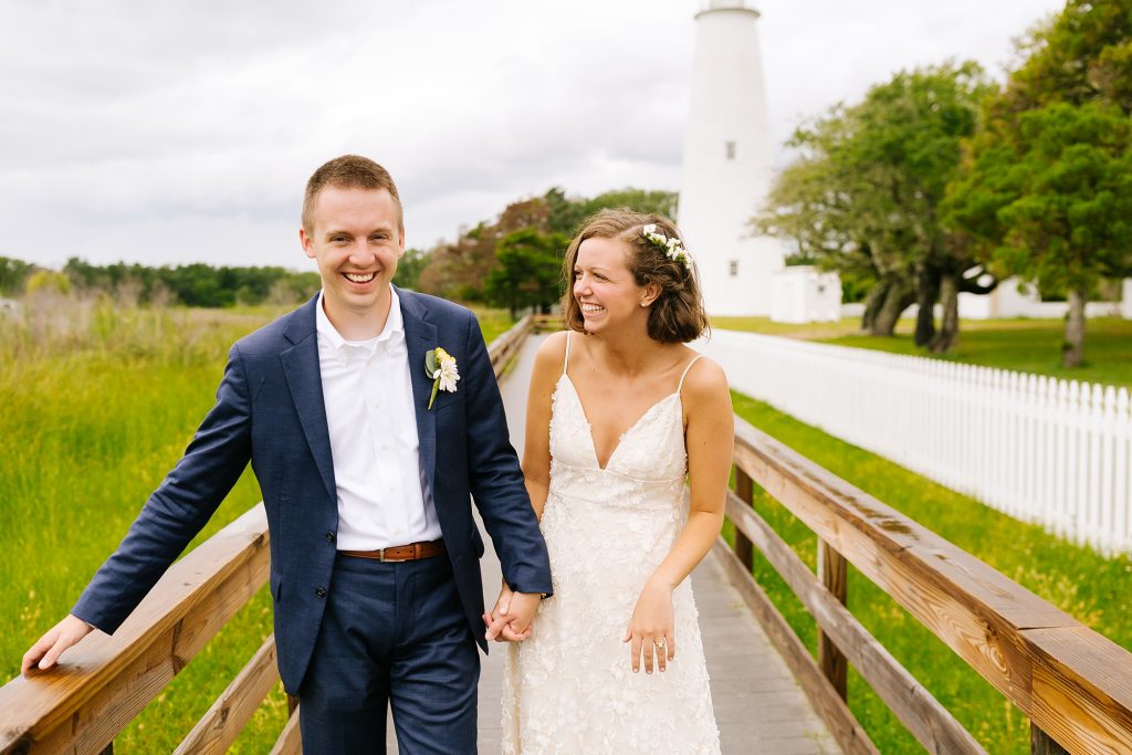 newlyweds laugh, walking in front of Ocracoke Lighthouse