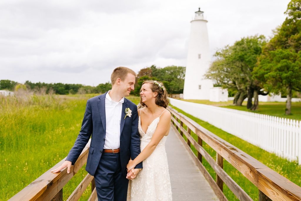 bride holds groom's hands standing in front of Ocracoke Lighthouse