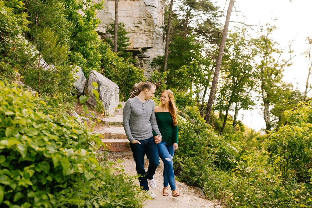 bride and groom walk through rock formation on mountainside during engagement session