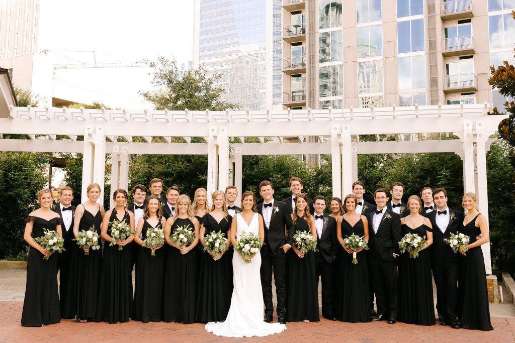 bride and groom pose with full wedding party in black dresses and tuxes