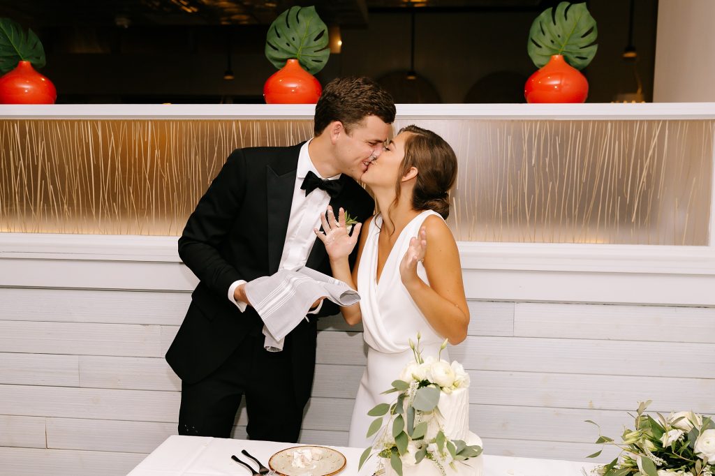 newlyweds kiss after cutting cake during Uptown Charlotte wedding reception