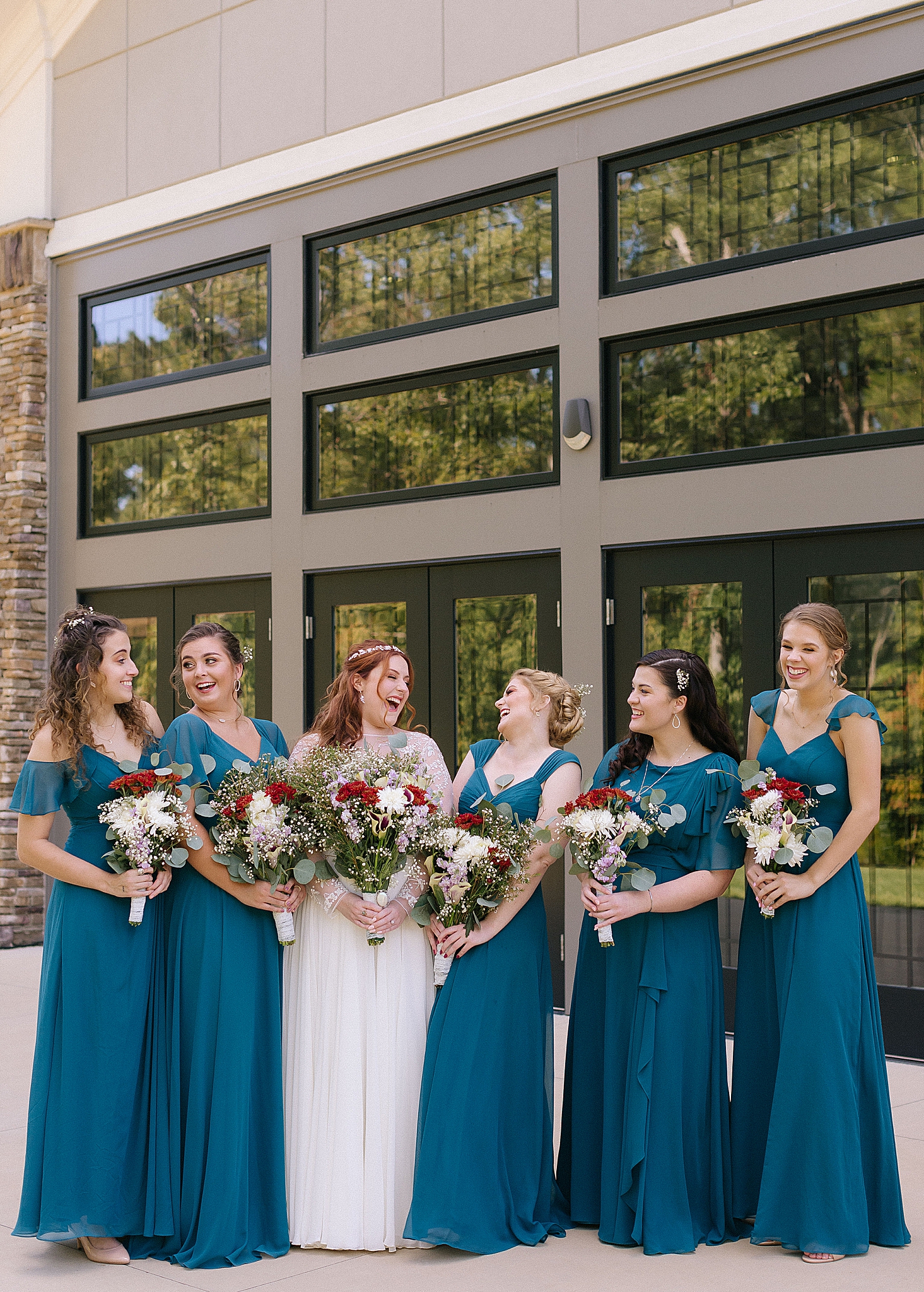 bridesmaids in teal gowns pose with bride outside Southern Charm Events