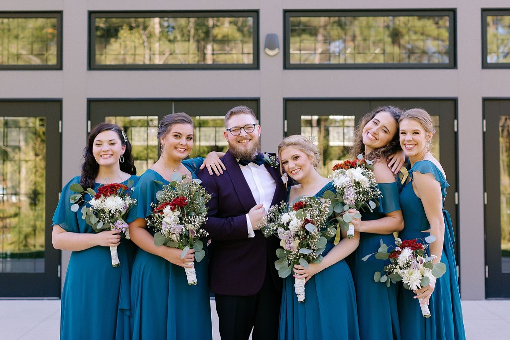 bridesmaids in teal gowns pose with groom
