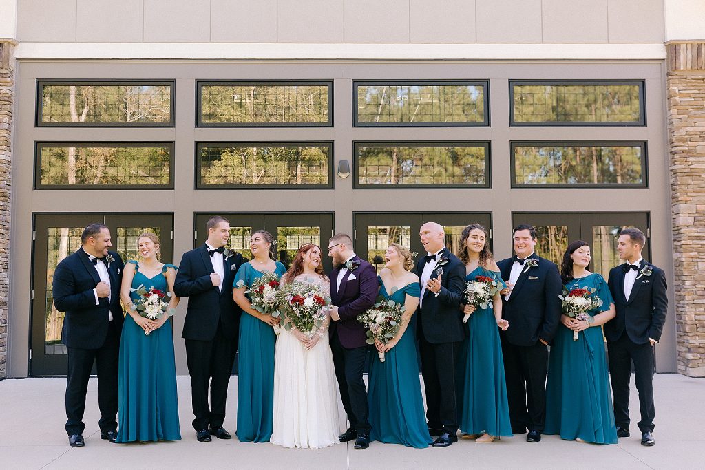 bridal party in teal gowns and black suits pose with bride and groom