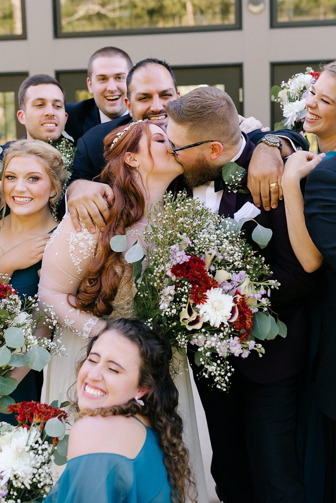 bride and groom kiss with bridal party around them