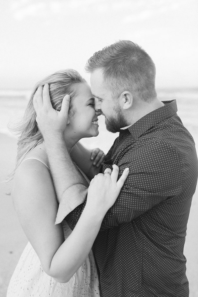 groom holds bride's hair back during beach engagement session