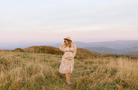 mom holds belly and brim of hat at Max Patch during Asheville maternity session