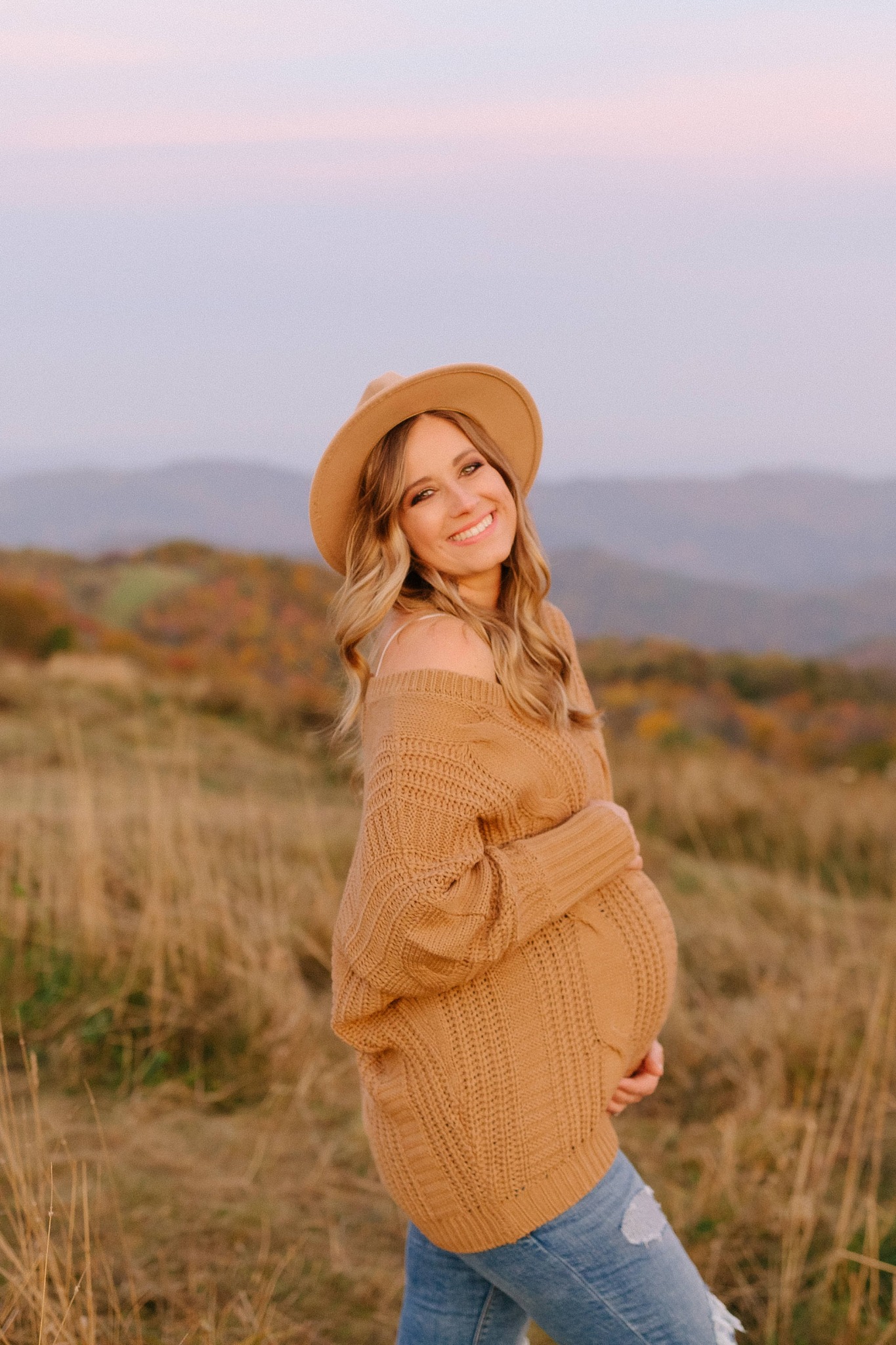 mom holds belly and laughs during maternity session on mountaintop 
