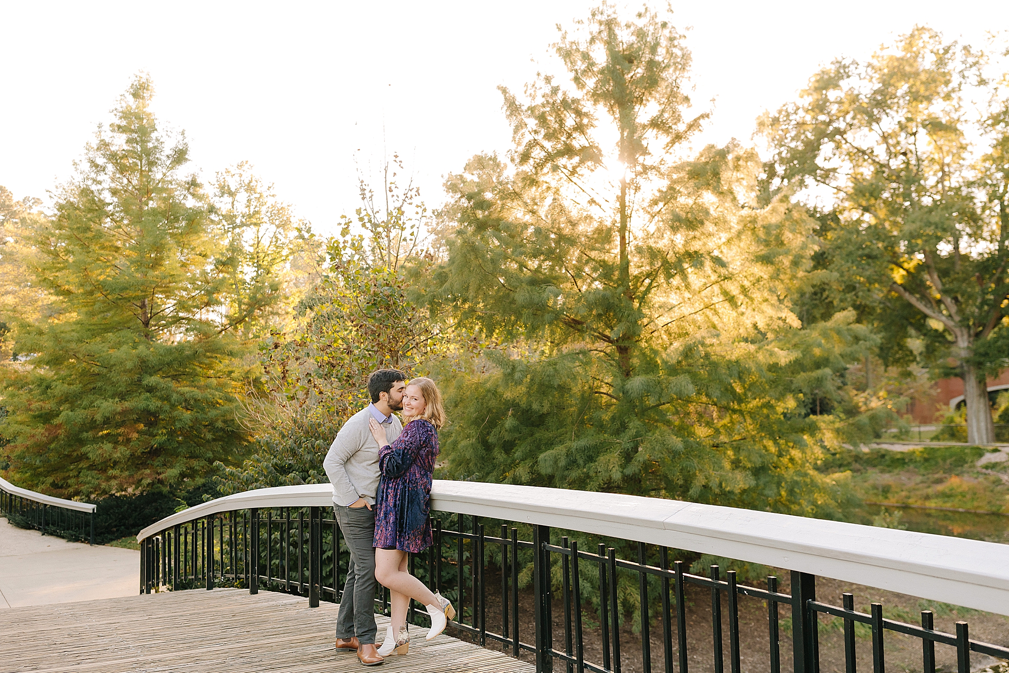 engaged couple poses on bridge in Pullen Park
