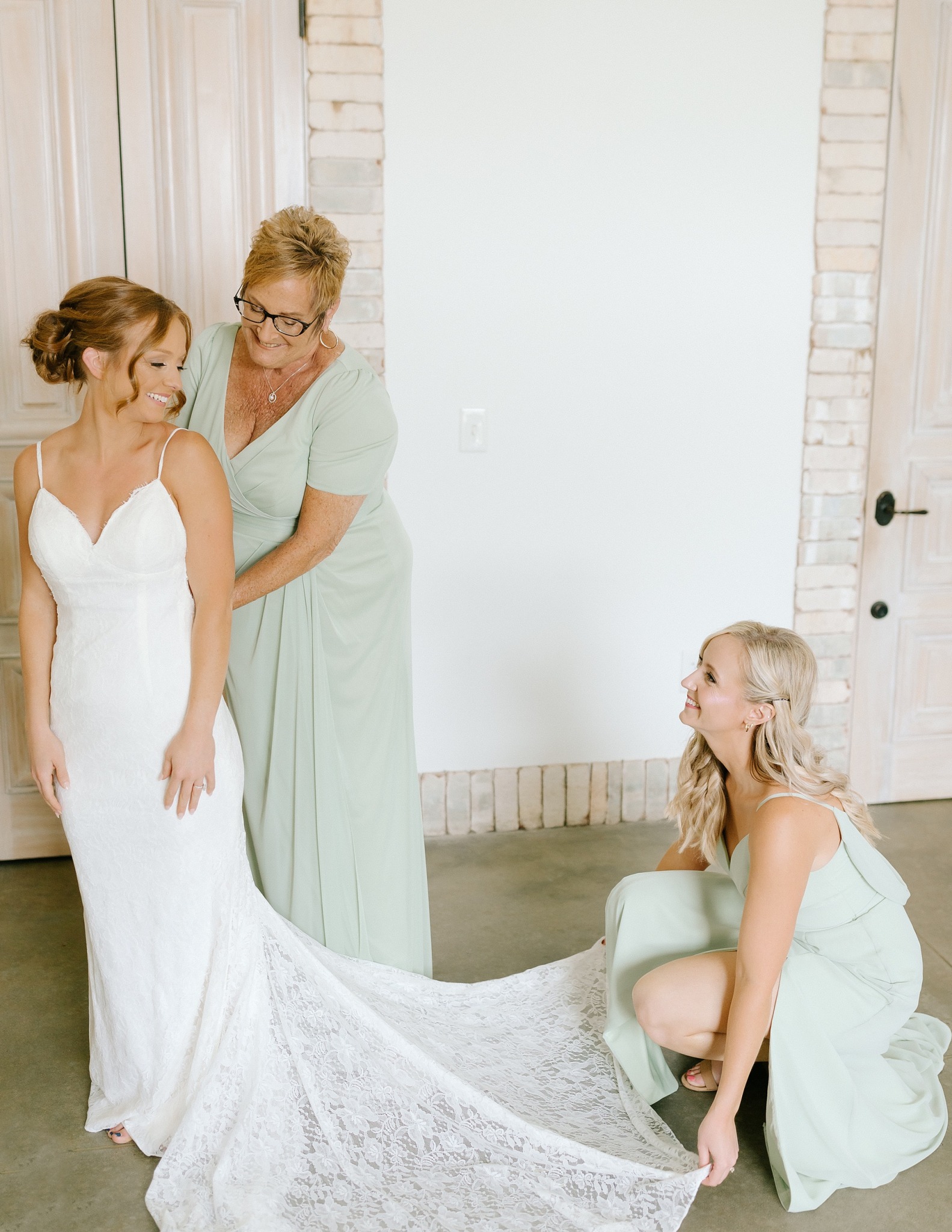 mother and sister help bride with wedding gown