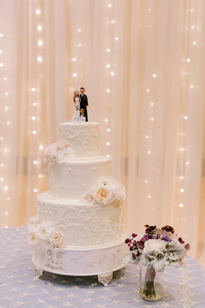 tiered wedding cake in front of cloth wall hanging with lights