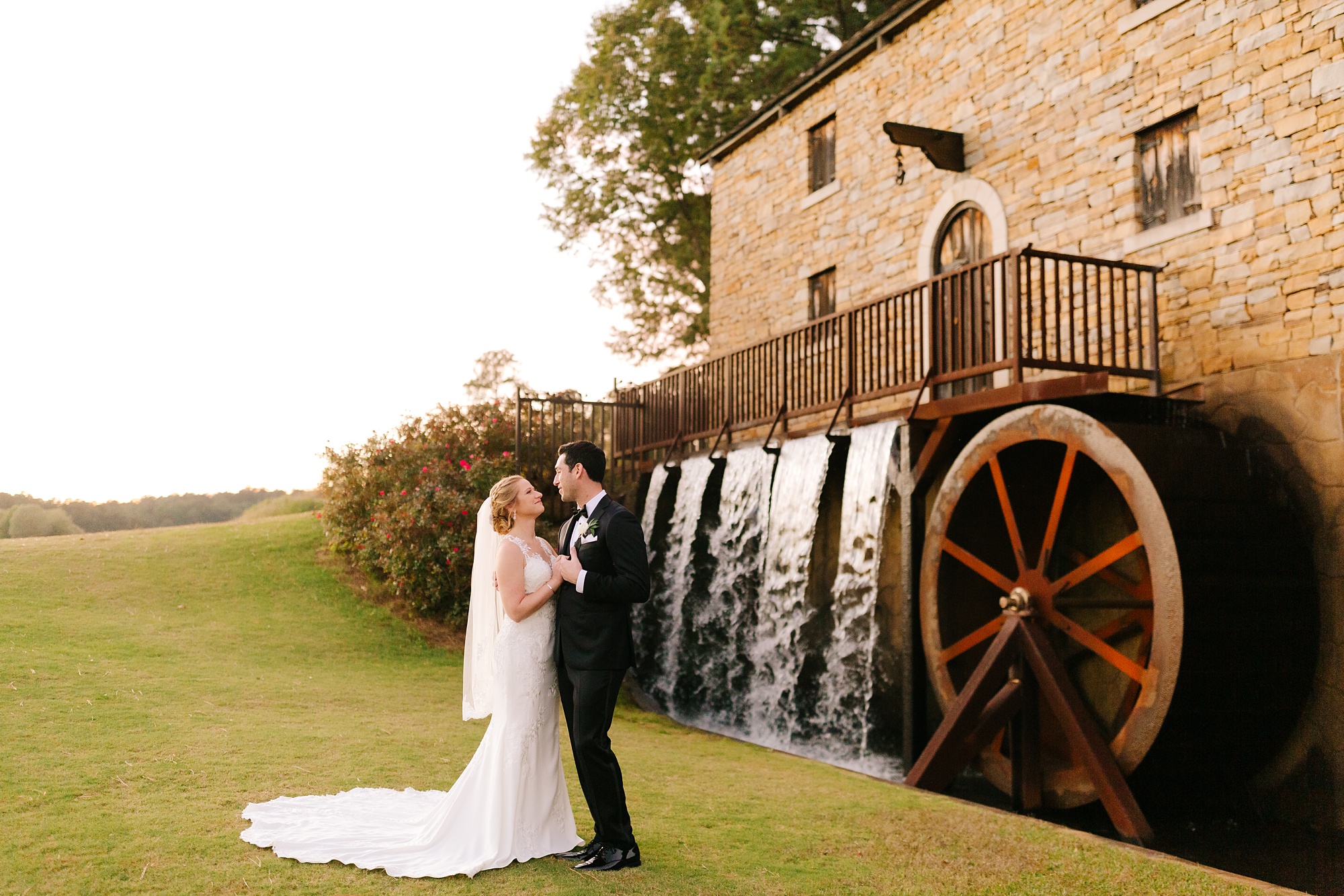 bride and groom pose by waterwheel at Renaissance Ross Bridge