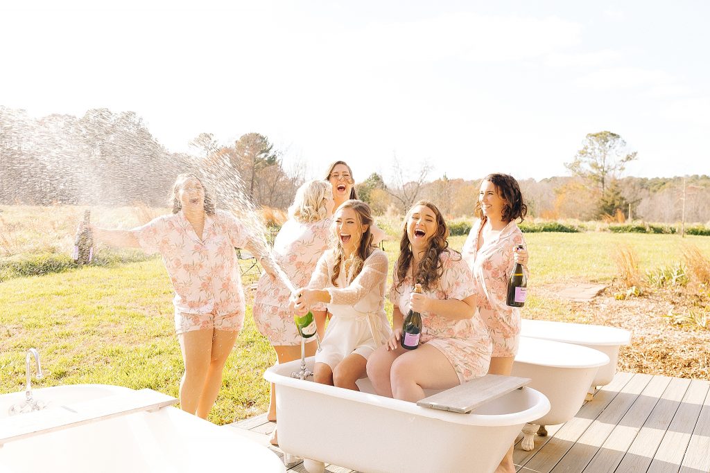 bride and bridal party pop Champagne in tub during wedding day prep