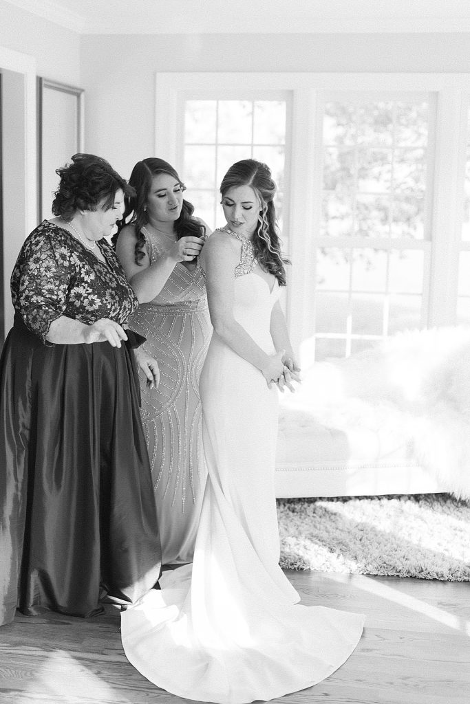 mother of bride and sister of bride help bride into wedding gown