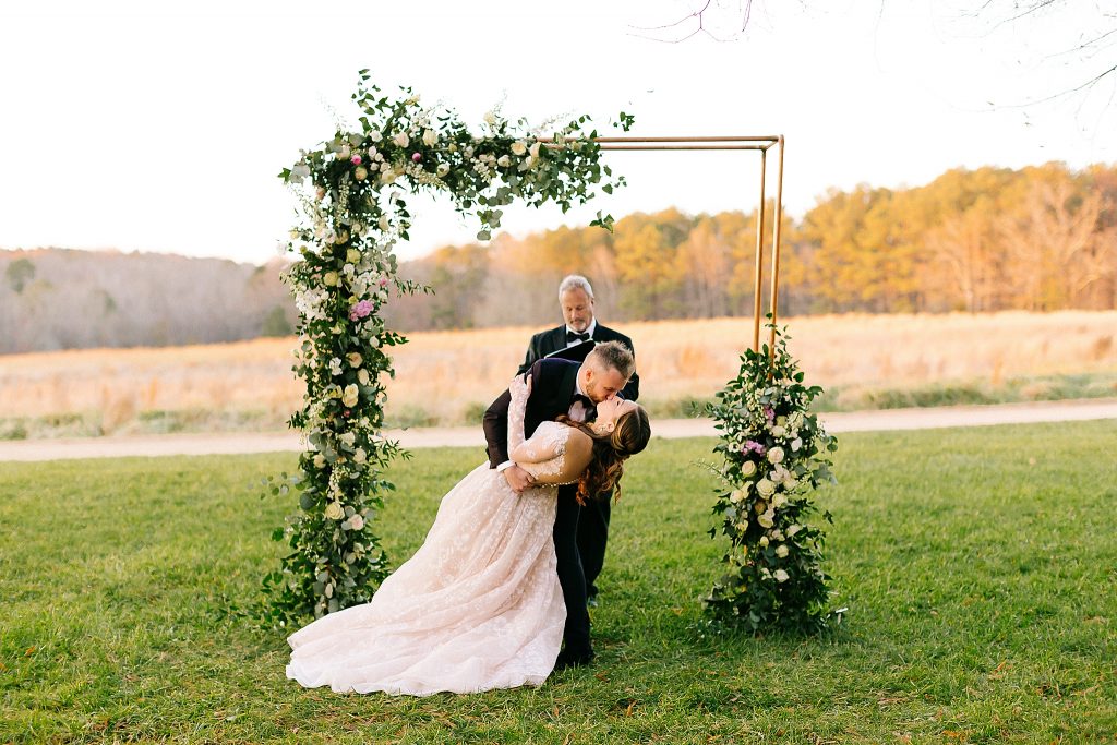 bride and groom kiss under golden arbor