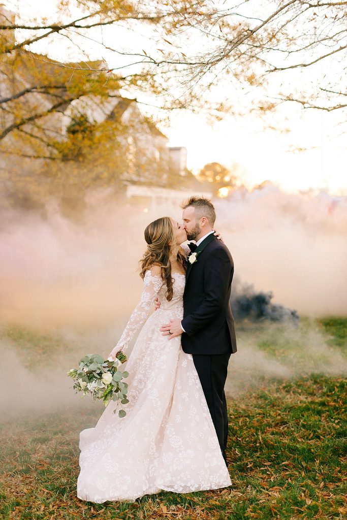 bride and groom kiss with pastel smoke bomb behind them