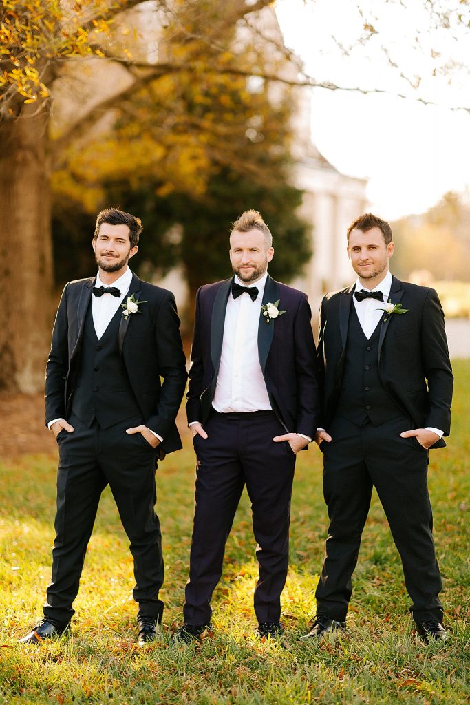groom and groomsmen pose with hands in pockets at The Meadows Raleigh