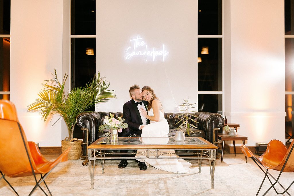 newlyweds pose on couch at The Meadows Raleigh under neon light of name
