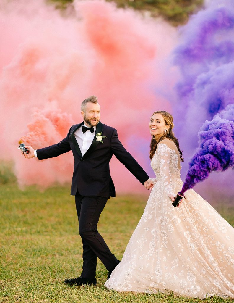 bride and groom walk with pink and purple smoke bombs at The Meadows Raleigh